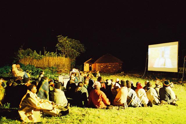 An audience sits on a grassy hill for an outdoor screening in a village in Africa. Courtesy of STEPS