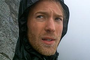 Close-up of a man wearing a windbreaker in front of a cliff