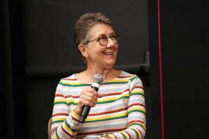 Julia Reichert, a white woman with short grey hair, glasses, and a striped shirt, participates in an on-stage conversation, presented in 2019 by IDA.. Photo: Laura Ahmed