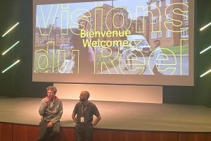Screen of a welcome sign for Visions du Réel. Two men standing in front of the screen, one on left is 'Pianoforte' director, Jakub Piatek.