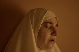 Still from 'Q.' Eyes closed, Hiba's face is softly lit against a light background, with a tear streaming down her cheek.