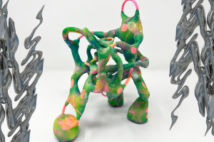 An art piece by Nat Decker: on the left and right edges of a green, pink, and orange twisted 3D sculpture that looks like it’s made of clay we see 3D iridescent dark grey chrome squiggles