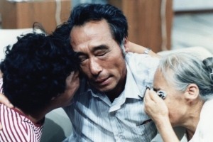 A middle-aged Korean man embraces two older Korean women as they cry