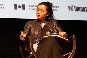 A person sits in a director's chair at a festival, holding a microphone.