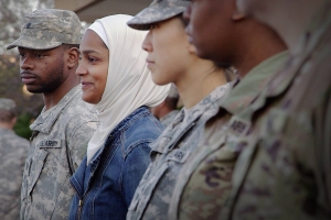 A Muslim woman wearing a hijab stands among a line of people in military uniforms