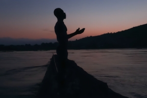 Film still from 'Eat Bitter,' showing the silhouette of a man with arms outstretched, on a small boat.