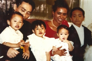 You see a blended Vietnamese and Amerasian family. There are 4 kids in the foreground. Three of them wearing White and one on the far left wearing a Black suit. The mother in the picture is wearing a red top with a pearl necklace.