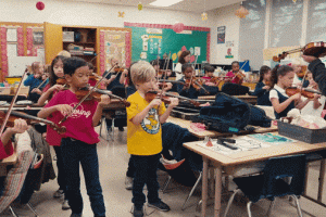A music teacher instructs a classroom full of second graders holding violins.
