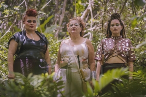 three people stand in a row in a jungle setting. they are wearing elaborate and beautiful outfits.