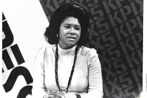 A black and white photograph of a woman with dark hair wearing a white top.