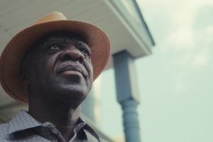 A Herero man wearing a straw hat looking beyond his front porch.