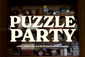 A wood cabinet with shelves full of mechanical puzzles. The puzzles are all manners of shapes and sizes, and crafted from a variety of materials. Text on the screen reads Puzzle Party, a film about the world of mechanical puzzles.