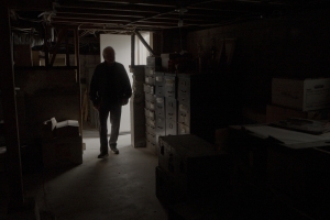 A man is silhouetted as he enters a basement filled with file cabinets and boxes.
