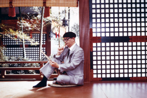 Osamu Tezuka (c. 1973) sits on the floor in a traditional Japanese room, observing a drawing, with a brush in his hand.