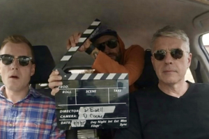A candid production still showing three members of the Paper Moon Rise team inside the car used during their Kansas road journey. Seated on the left is on-screen talent Harry Cooke, in the center is Director of Photography David Coone holding the film slate, and on the right is producer/director David Ezell at the wheel. The image captures the spirit of a small crew on the road, documenting the landscapes and communities at the heart of the film.