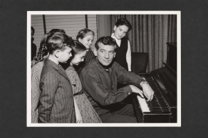 Leonard Bernstein playing the piano with a group of young children.