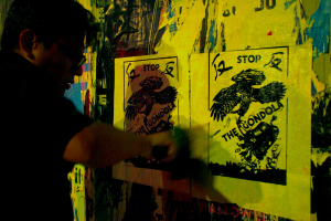 A shadowy figure wheatpastes a flyer on a wall.