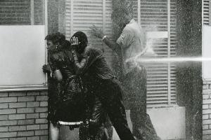 Black and white film still from 'Mighty Time Volume 2: The Children's March' of three Black people being hit with a high-pressure hose on the sidewalk. Courtesy of Tell the Truth Pictures
