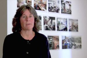 A woman talks in front of a wall of photos.