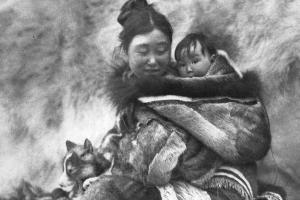 A woman smiles while looking towards the baby she's carrying on her back. From Robert Flaherty's 'Nanook of the North' (1922).