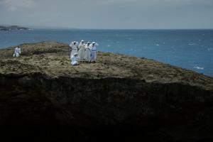 Seis monjas con sus hábitos blancos de pie en tierra, el océano a su alrededor. Del filme 'Landfall' por Cecilia Aldarondo. Cortesía de Cecilia Aldarondo