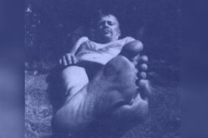 A man looks down at the camera with his foot in the forefront of the frame, from Tahvo Hirzonen's <em>Tino</em>.