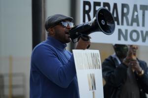 A Black man, wearing a blue polar fleece, leads a protest calling for reparations for victims of the 1921 Tulsa Massacre.
