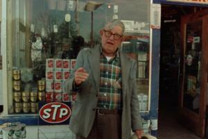  An older man with glasses and gray hair wearing a plaid shirt and blazer stands outside a storefront. He points at the camera while talking. From Errol Morris' Vernon, Florida. Courtesy of Criterion Collection. 
