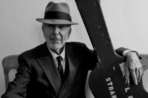 An image from Hallelujah: Leonard Cohen, A Journey, A Song, Leonard Cohen is wearing a fedora and holding a guitar in a black & white photo. 