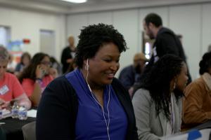 A Black woman in blue shirt and black cardigan, listening to her headphones sitting down