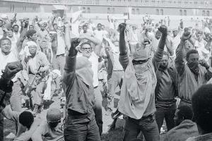 A black and white picture of a group of men with their firsts raised in the air.