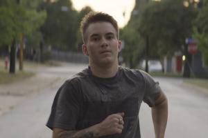 A man with white skin and short blond hair runs down a street.