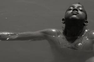 A black and white picture of a boy with Black skin swimming in water.