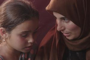 A woman in a brown hijab talks to a little girl.