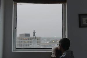 A man stares out the window at a large statue of a person.