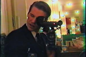 A white man with short brown hair holds a camera up to a mirror.