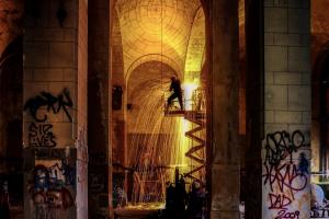 a man welds in the graffitied arches of what appears to be an old church. 