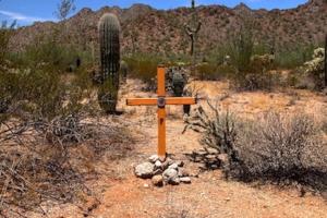 An artistic orange cross propped up with stones in the Sonoran Desert