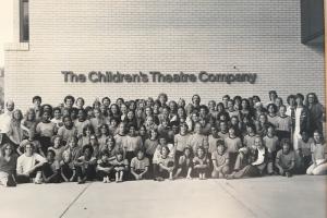 A black and white class photo in front of a building named "The Children's Theater Company"