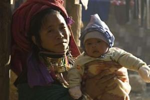 An Asian woman in an elaborate headscarf and necklaces holds her infant child.
