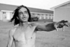 Black and white photograph of a shirtless Native American man reaching his arm out in mid-speech
