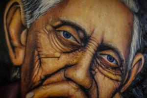 A close-up of a painting of a wrinkled face of an old woman.