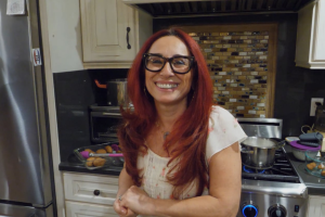 A red-haired Armenian-American smiles at the camera in a home kitchen.