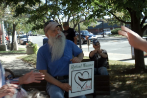 A white man with a beard holds an anti-refugee sign in a residential neighborhood.