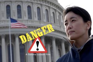 An Asian woman in a windcoat stands in front of the US Capitol.