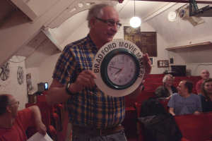 A man holding green clock that is labeled 'Bradford Movie Makers'