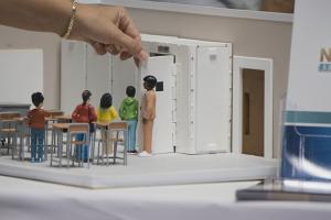 hand of person uses small replica of school classroom to teach gun related safety protocols