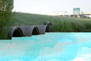 young boy sitting on top of one of three drainage tunnels expelling blue water color paint