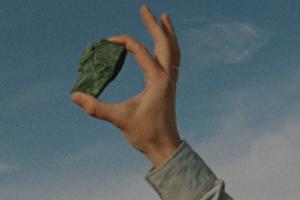 A rock held up to the sky between the index and thumb of a masculine hand