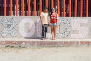 Two people are standing in front of a wall that has 'xolos' graffitied on it.